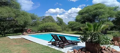 a swimming pool with two chairs and a fire place at Vaalkop Dam Reserve, self-catering log cabin holiday home in Beestekraal, South Africa in Beestekraal