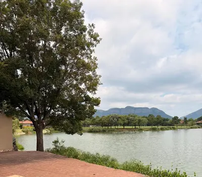 a tree next to a lake with mountains in the background at Lakeview Haven in Hartbeespoort