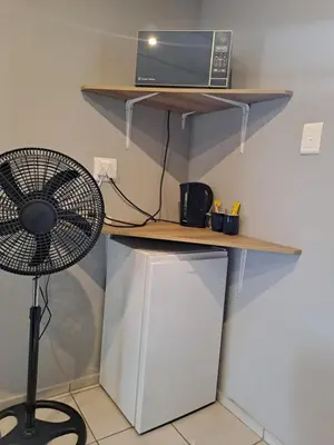 a desk with a fan and a microwave on a shelf at Close to O R Tambo Airport Alderlane 1 in Kempton Park