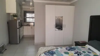 a white room with a bed and a kitchen at Ermelo Executive Rooms in Ermelo