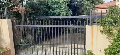 a gate to a driveway with trees and bushes at Villa at Wekker Upstairs in Pretoria