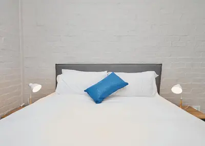 a white bed with a blue pillow on it at Brooklyn Modern Apartment Near Hatfield & Menlyn in Pretoria