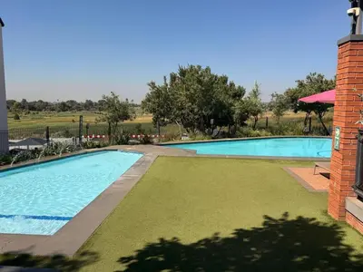a swimming pool with green grass next to a building at GreenPark Home A chic retreat and peaceful home in Boksburg