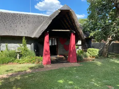 a house with a thatched roof with red curtains in the doorway at Dorpsrus in Bela-Bela