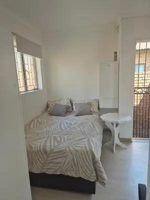 a white bedroom with a bed and a table at TALOEM Private Room in Pretoria