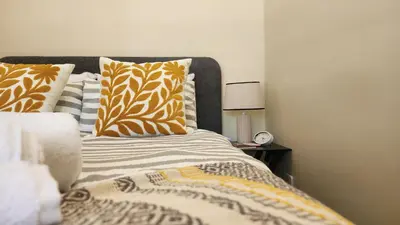 a bed with orange and white pillows and a clock at Elegant Self-Catering Witbank, 6 min Highveld Mall in Witbank