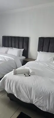 a bedroom with two beds with white sheets and a headboard at Good night guest house in Polokwane
