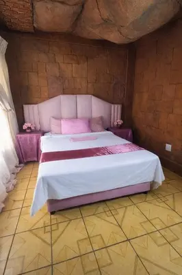 a bedroom with a large bed with pink sheets at Ndou The Rocks Lodge in Hammanskraal Station