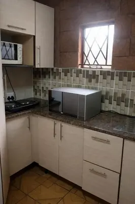 a kitchen with white cabinets and a microwave at Ndou The Rocks Lodge in Hammanskraal Station