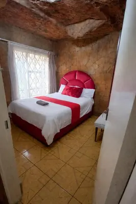 a bedroom with a bed with a red headboard and a window at Ndou The Rocks Lodge in Hammanskraal Station