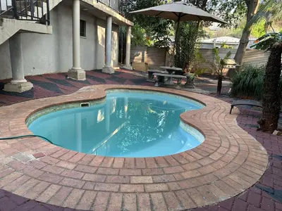 a swimming pool on a brick patio with an umbrella at 373 Guest House in Pretoria