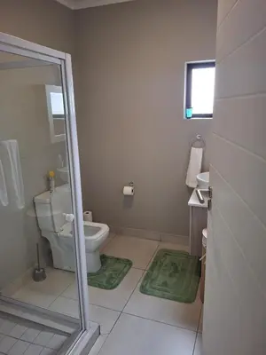 a bathroom with a toilet and green rugs at Oak and Olive Retreat Midrand in Midrand