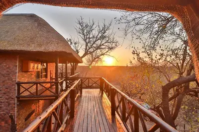 a bridge leading to a hut with the sunset in the background at Inyathi in Marloth Park