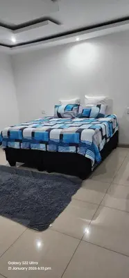 a bed in a white room with a blue blanket at Thohoyandou P house rooms in Thohoyandou