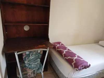 a small bedroom with a bed and a wooden chair at Roullas gardens in Pretoria