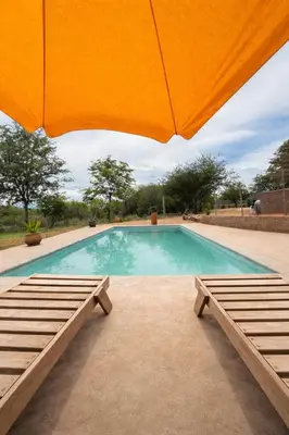 a swimming pool with an umbrella and two benches at Mathendele Bush Lodge in Oporto