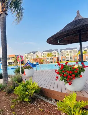 a wooden deck with flowers and an umbrella next to a pool at 1 Bedroom Apartment at The Blyde, Pretoria in Pretoria