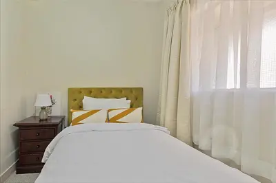 a white bedroom with a bed and a window at Calmwood Stay in Midrand