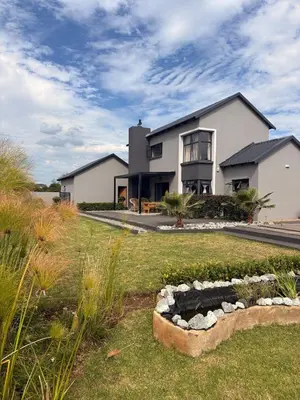 a large white house with a landscaped yard at 202 on Crescent - Luxury Wildlife Escape in Hartbeespoort with Magaliesberg Mountain views in Hartbeespoort