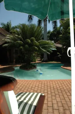 a swimming pool with a green umbrella and a bench at Trees Too Guest Lodge in Komatipoort