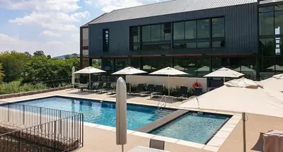 a large building with a swimming pool with umbrellas at Home away from home in the heart of waterfall in Midrand