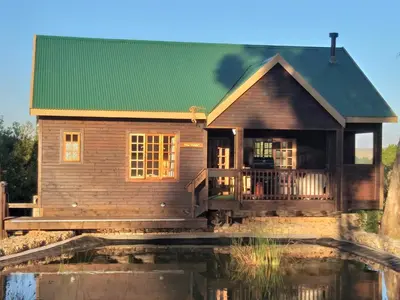a wooden house with a green roof next to a body of water at Kliphuisjes in Dullstroom