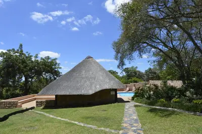 a hut with a thatched roof next to a pool at White House Lodge in White River