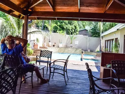 a man sitting on a deck near a swimming pool at Acacia Guest House in Nelspruit
