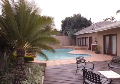 a pool with chairs and a palm tree next to a house at Acacia Guest House in Nelspruit
