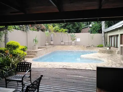 a swimming pool with two chairs and a table at Acacia Guest House in Nelspruit