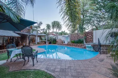 a swimming pool in a yard with two chairs and a table at Kassaboera Lodge in Hartbeespoort