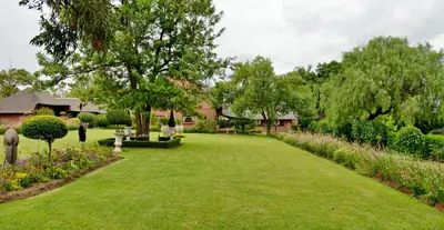 a garden with green grass and flowers and a house at Owls Loft Guest House in Midrand