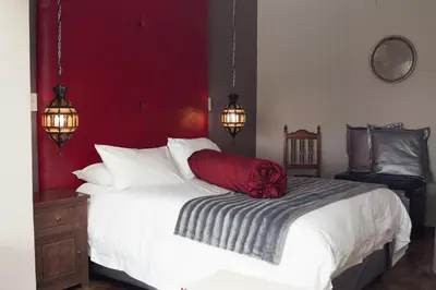 a bedroom with a white bed with a red wall at Annie's Boutique Guesthouse and Garden Spa in Hartbeespoort