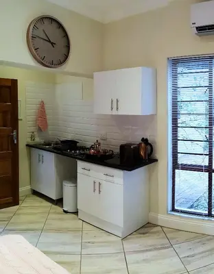 a kitchen with white cabinets and a clock on the wall at Andante Lodge in Pretoria