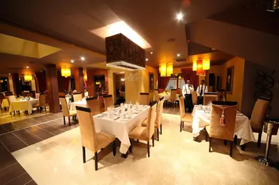 a dining room with white tables and chairs and a man standing at Cycad Guest House in Polokwane