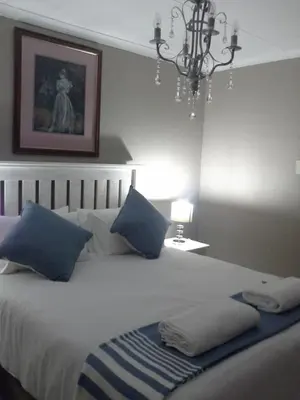 a bedroom with a bed with blue pillows and a chandelier at De Zevende Hemel Guesthouse in Secunda