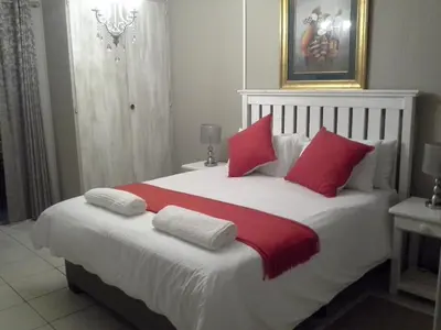 a bedroom with a large white bed with red pillows at De Zevende Hemel Guesthouse in Secunda