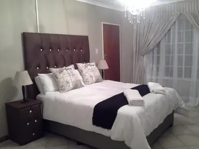 a bedroom with a large bed and a chandelier at De Zevende Hemel Guesthouse in Secunda