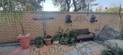 a wooden bench next to a brick wall with a cross at De Zevende Hemel Guesthouse in Secunda
