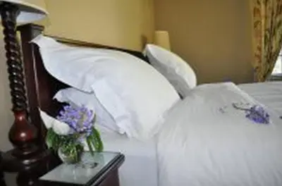 a bed with white pillows and a table with flowers on it at Plumbago Guest House in Hazyview