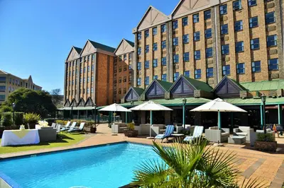 a pool with chairs and umbrellas in front of a hotel at The Centurion Hotel in Centurion