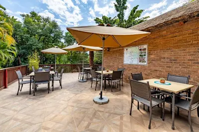 a patio with tables and chairs and umbrellas at Woodlands Guest House in Hazyview