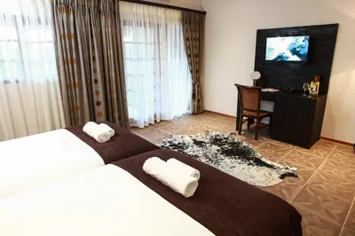 a hotel room with a bed and a desk and a television at Woodlands Guest House in Hazyview