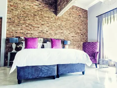 a bedroom with a brick wall and a bed with purple pillows at Rustique Boutique Hotel in Middelburg