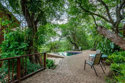 a patio with a table and chairs next to a pool at Blue Jay Lodge in Hazyview
