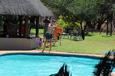 a young man standing next to a swimming pool at Re a Lora Lodge in Bela-Bela