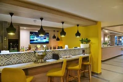 a bar in a restaurant with yellow walls and yellow chairs at Town Lodge Menlo Park in Pretoria