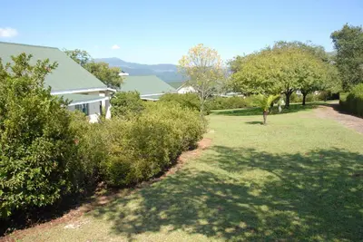 a yard with bushes and trees and a house at Kloofsig Holiday Cottages in Graskop