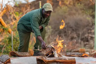 a man standing over a fire with a knife at Baobab Hill House by RETURN Africa in Makuleke Contract Park