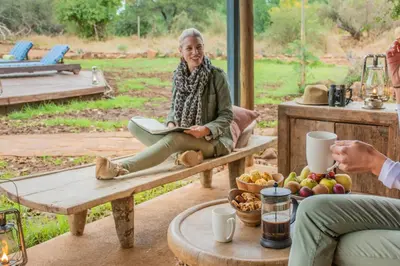 a woman sitting on a bench with a book at Baobab Hill House by RETURN Africa in Makuleke Contract Park